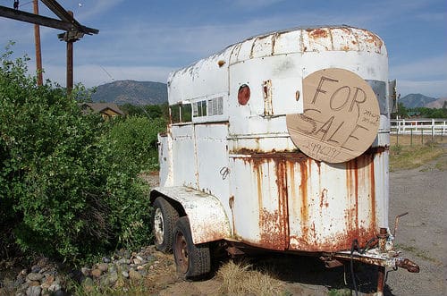 Rusted white stock trailer with a cardboard for sale sign