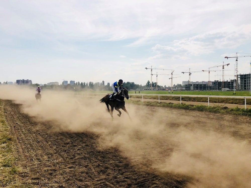 an image of a horse race on a dirt track with a lot of dirt stirred up and the horse and jockey in the far background