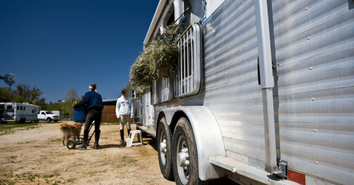 Aluminum horse trailer with people tending hay standing next to it