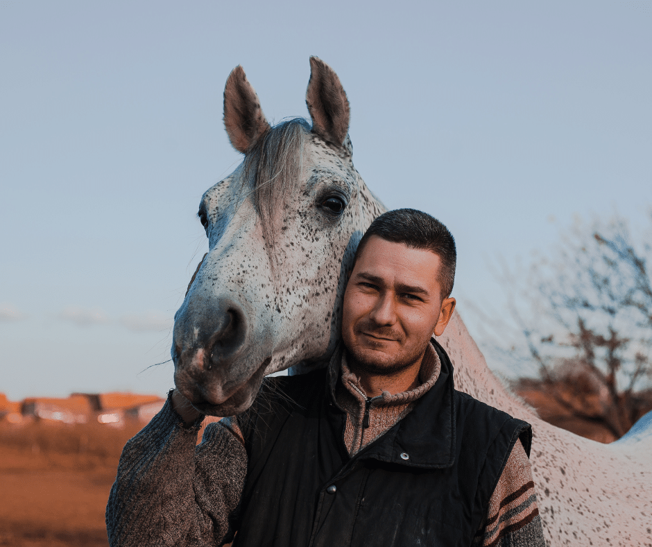 a horse owner standing with his horses head on his shoulder