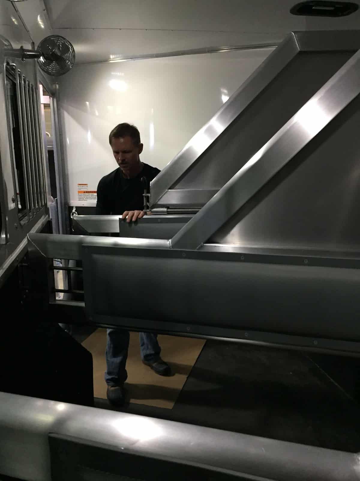 D. Brad Heath inspecting a dark and cramped side load horse trailer interior.