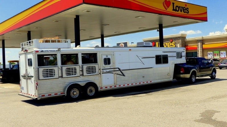 a 3 horse trailer behind a truck parked at a gas station