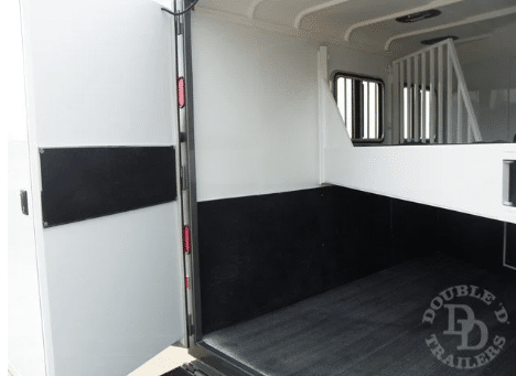 The inside of a Double D bumper pull horse trailer showcasing ventilation fans, mats, and dividers.