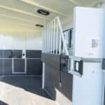 The interior of a horse trailer with a partition, padded walls, rubber flooring, and an open side door, designed for safely transporting horses.
